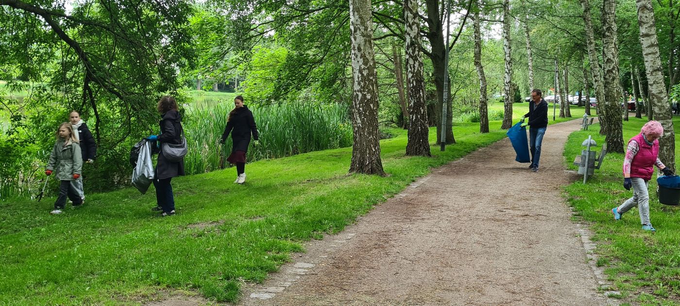 Erwachsene und Kinder sammeln mit Greifern Papier im Stadtpark.