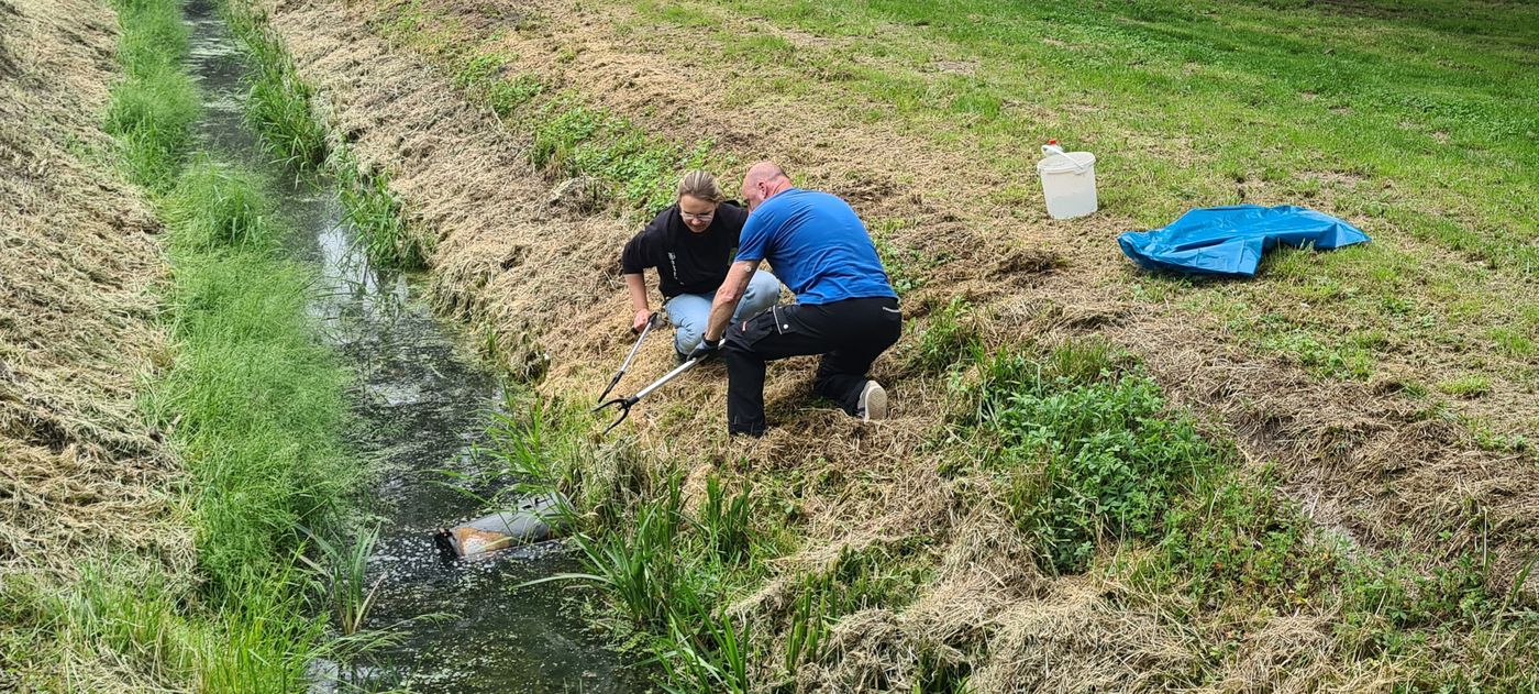 Zwei Müllsammler bergen eine alte Tonne aus einem Wasserlauf.