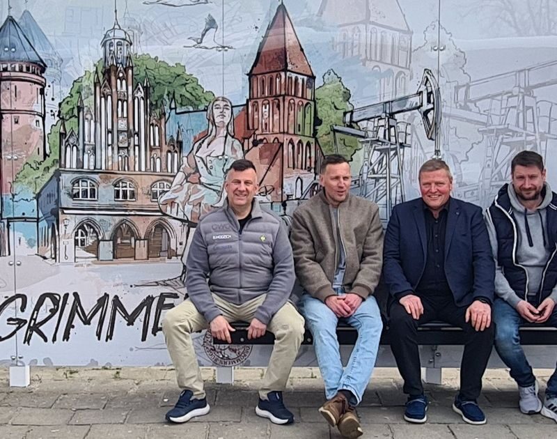 Bürgermeister Marco Jahns, Künstler Christoph Kadur, GWG Technikleiter Björn Wodzich und Werbefachmann Reno Zülsdorf sitzen in der neu gestalteten Busbude am Bahnhof. Im Hintergrund, ist die neue Graftik der Stadt Grimmen zu sehen.