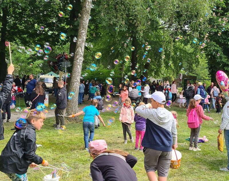 Kinder spielen auf einer Wiese mit großen Seifenblasen.
