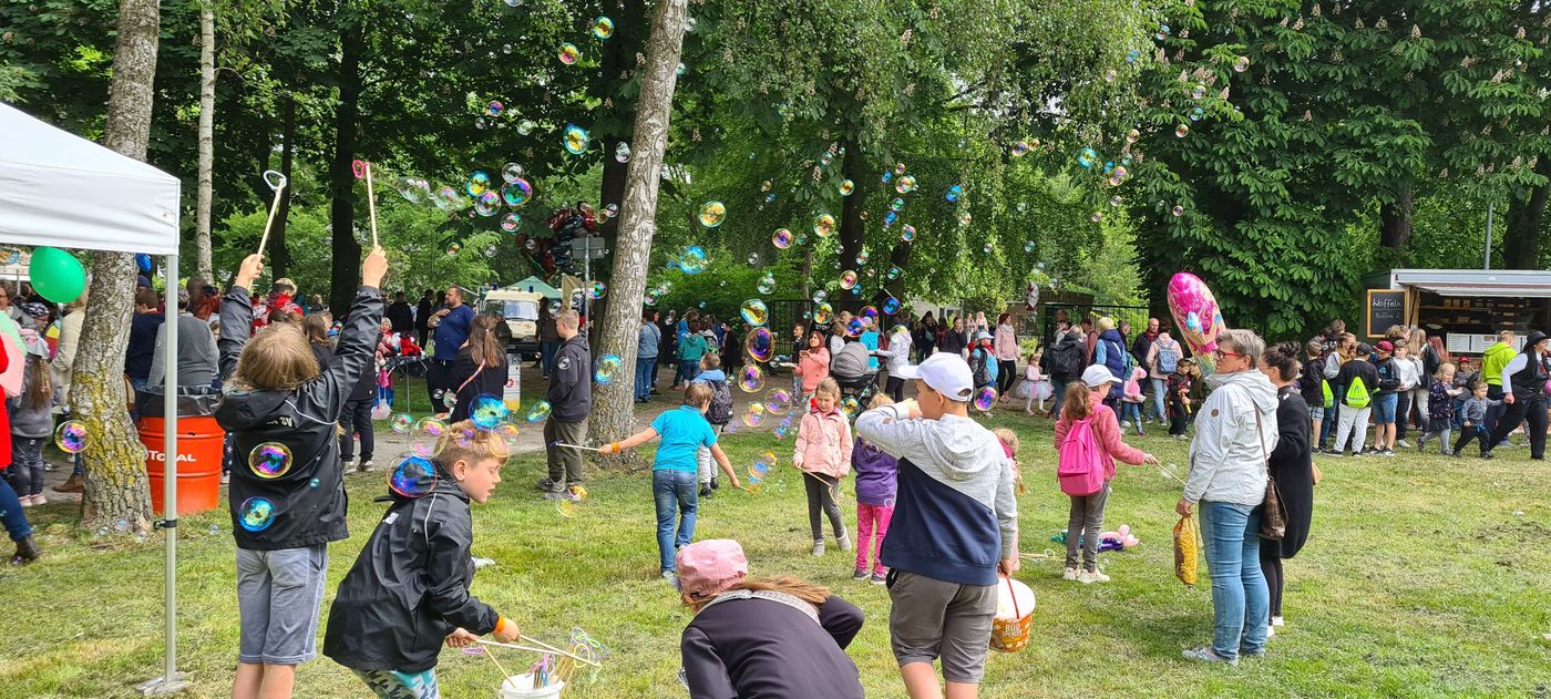 Kinder spielen auf einer Wiese mit großen Seifenblasen.