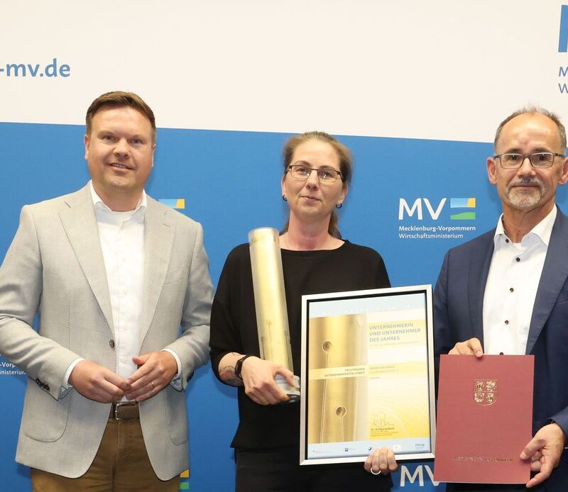 Mareen Buchholz erhält den Preis von Wirtschaftsminister Wolfgang Blank. Sie lächelt mit der Urkunde in der Hand in die Kamera.