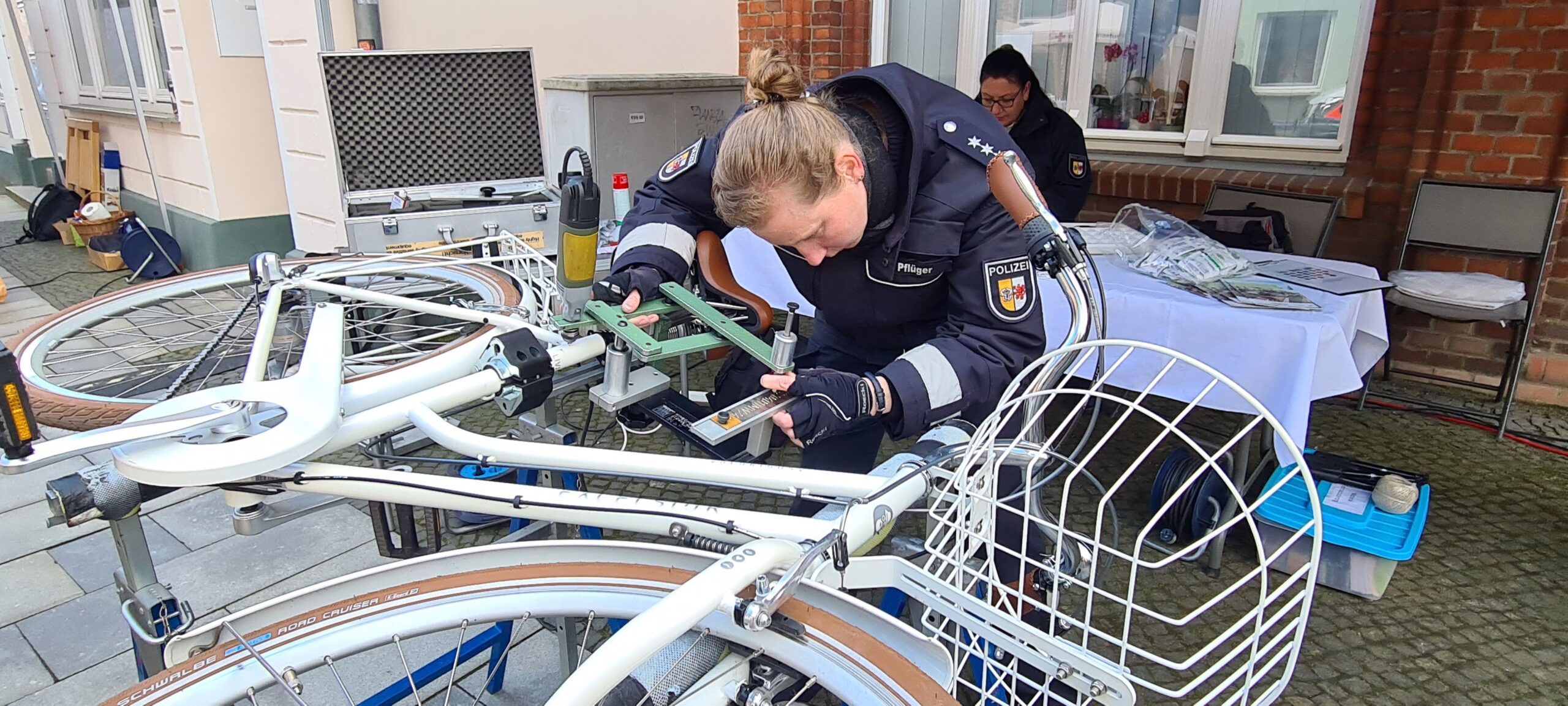 Polizistin beugt sich über ein auf der Seite liegendes Fahrrad. Mit einer Fräse codiert sie den Fahrradrahmen.