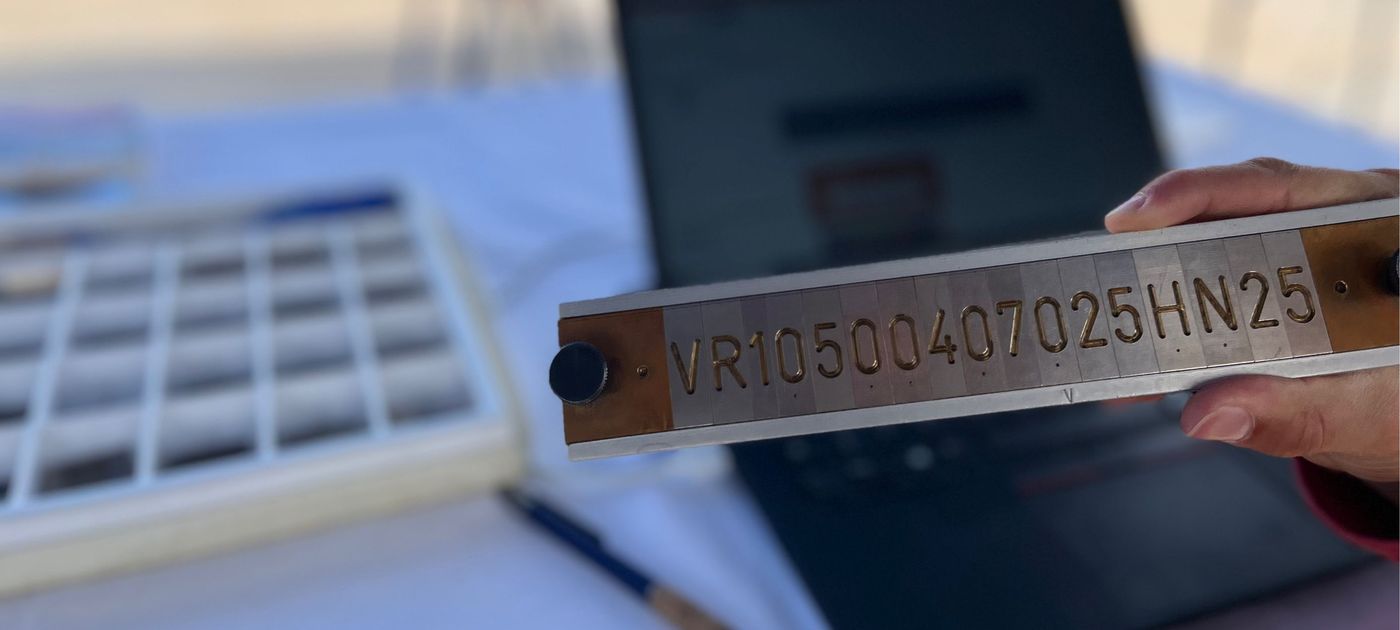 Eine Beamtin zeigt eine Schablone mit einer Nummer, die als Vorlage für die Fräse dient.