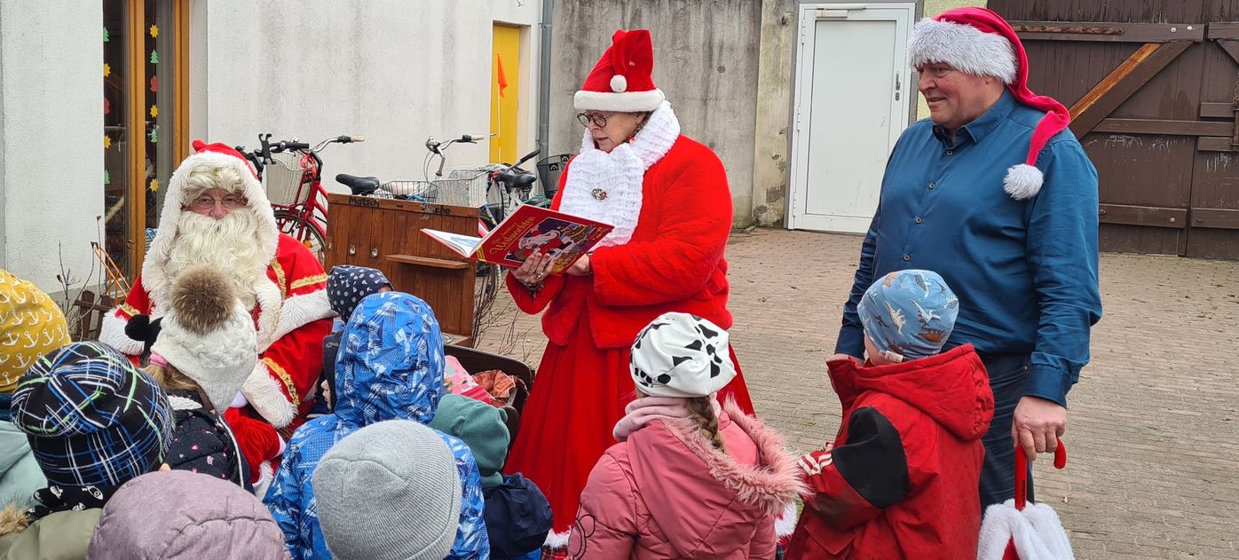 Auf dem Hof der Kita "Kinderkahn" stehen die Kinder und umringen den Weihnachtsmann und Bürgermeister. Märchantante Nicolina liest eine Geschichte vor.