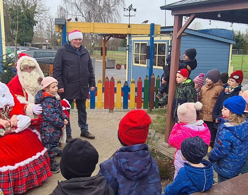 Der Weihnachtsmann und die Märchentante sitzen auf einer bank. Der Bürgermeister steht daneben. Die Kinder blicken gespannt zu den dreien und lauschen einer Geschichte.