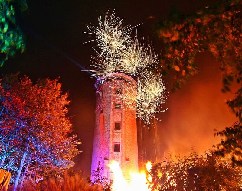 Grimmener Wasserturm im bunten Scheinwerferlicht. Zu sehen sind pyrotechnische Effekte des Feuerwerkes.