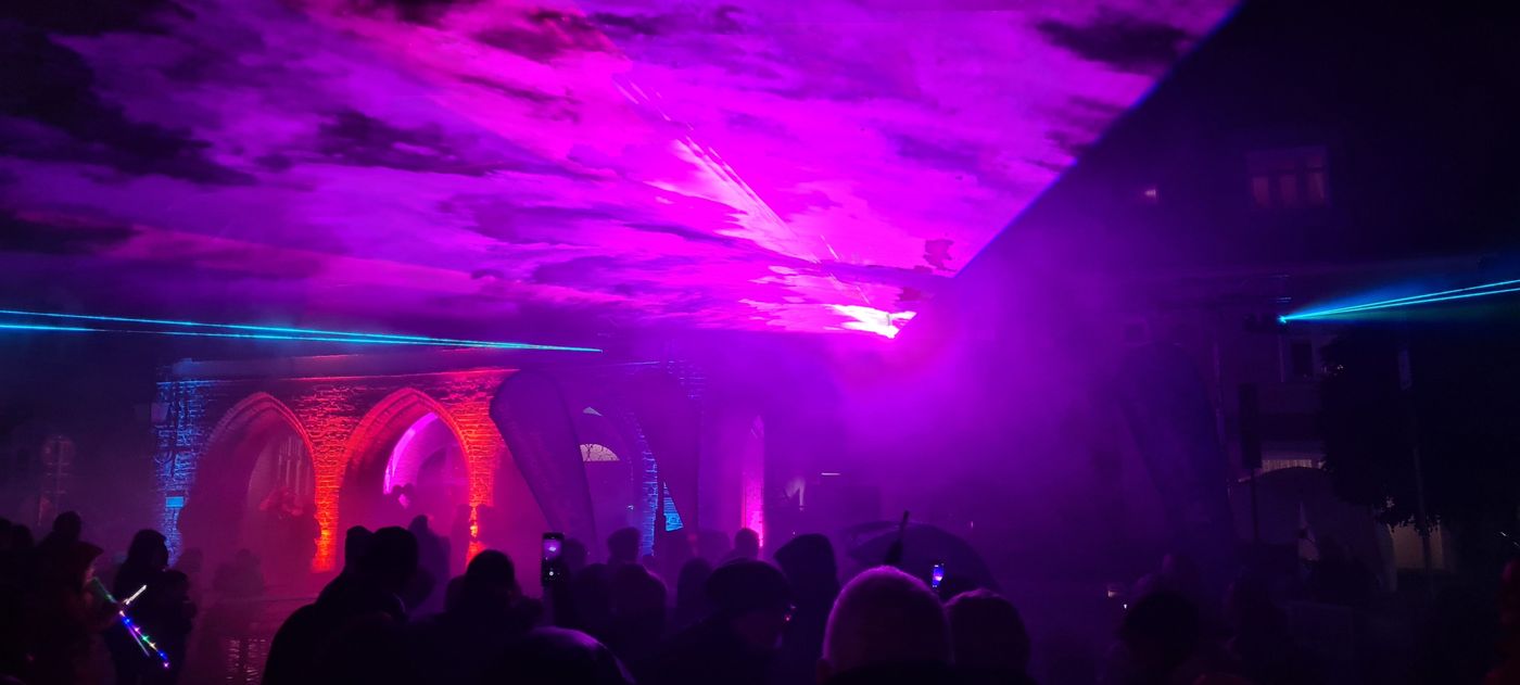 Lasershow auf dem Marktplatz. Zu sehen ist ein bunter Lichtkegel in dem Menschen stehen.