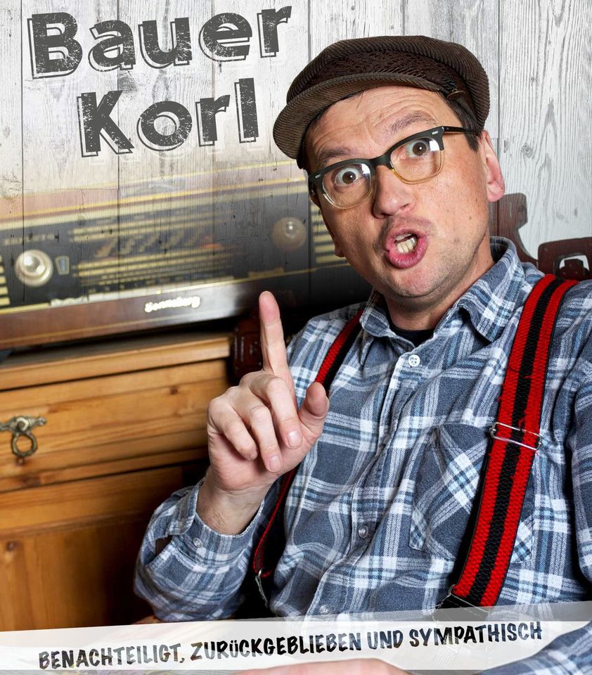 Ein Mann mit Brille, kariertem Hemd, roten Hosenträgern und einer braunen Mütze gestikuliert mit erhobenem Zeigefinger. Oben steht Bauer Korl und unten: BENACHTEILIGT, ZURÜCKGEBLIEBEN UND SYMPATHISCH.
